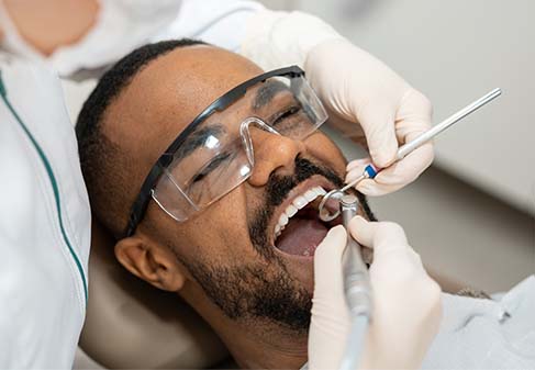 Man laying in operatory chair with dentist holding tools in mouth.